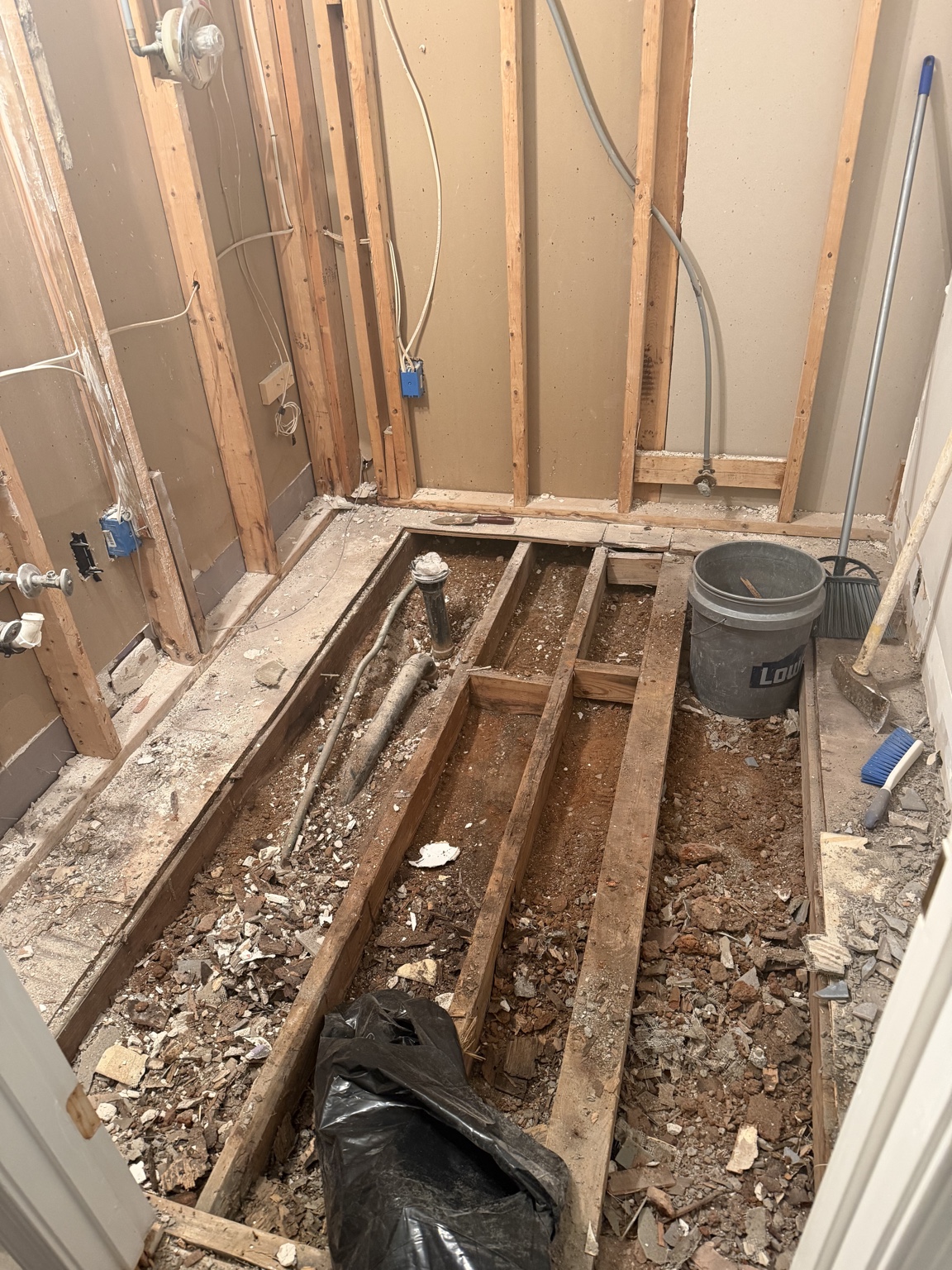 Bathroom floor removed to expose framing, plumbing, and red clay